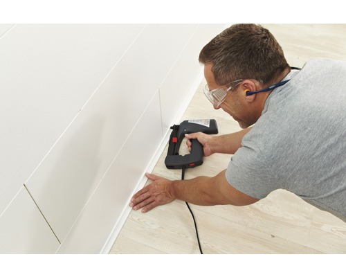 Mann befestigt Sockelleiste mit einem Elektrotacker an einer Wandpaneele.