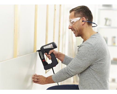 Mann befestigt Wandpaneele mit einem elektrischen Tacker an einer Wand