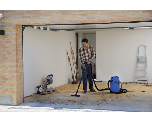 Mann saugt Späne in einer Garage mit einem Industriesauger