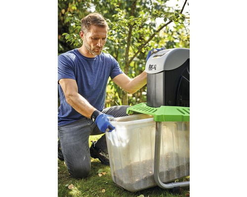 Ein Mann leert einen Behälter eines Gartenhäckslers in einem Garten.
