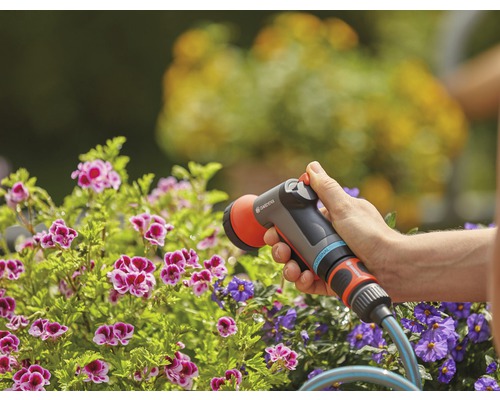 Gartenszene mit einer Person, die mit einer Gardena Gartenspritze Blumen gießt.