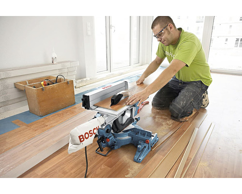 Ein Mann benutzt eine Kapp- und Gehrungssäge, um Holzboden zu schneiden, mit Werkzeugkasten und Holzlatten im Raum.