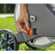 Detailaufnahme einer Hand, die eine orangefarbene Arretierung an einem Gartenschlauchwagen betätigt.