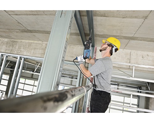 Handwerker bohrt mit einer Bohrmaschine in ein Metallprofil auf einer Baustelle.