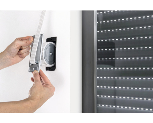 Person befestigt einen Gurtwickler für Rollläden an der Wand