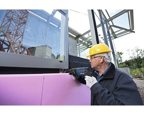 Handwerker schneidet mit einer Säbelsäge eine Dämmplatte an einem Gebäude zu.