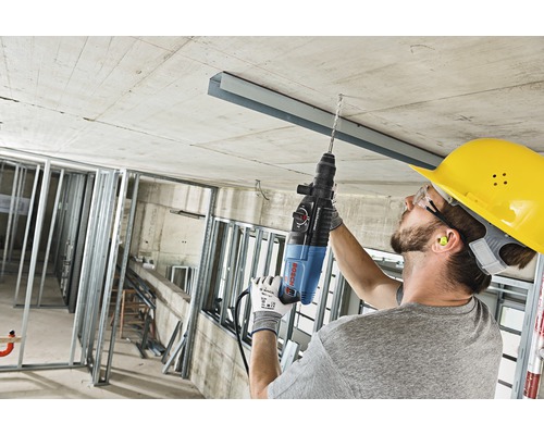 Ein Handwerker bohrt mit einem Bohrhammer in eine Betondecke auf einer Baustelle.