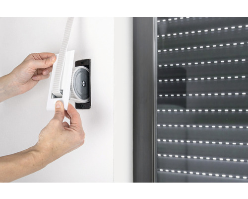 Eine Person montiert einen Gurtwickler für Rollläden an einer Wand neben einem Fenster.