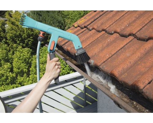 Eine Person reinigt eine Dachrinne mit einer Dachrinnenbürste und einem Gartenschlauch.