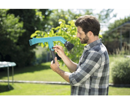 Mann bedient eine Dachrinnenbürste im Garten.