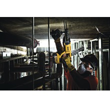 Ein Bauarbeiter bohrt mit einem Bohrhammer in eine Decke. Die Rohre und die Metallkonstruktion sind sichtbar.