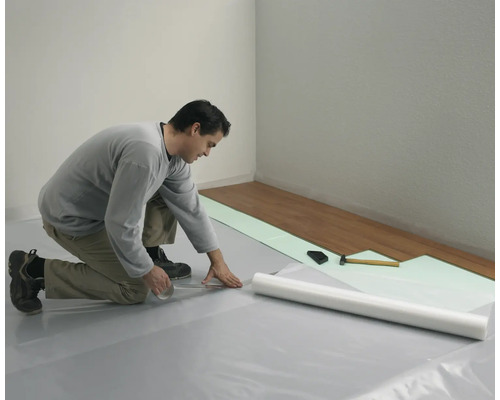 Mann verlegt Laminatboden mit Unterlagsbahn und Werkzeugen