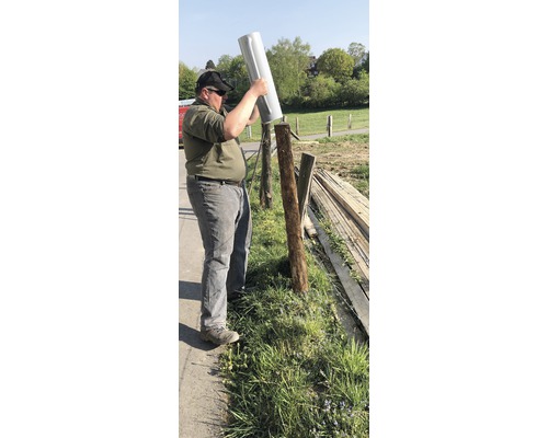 Eine Person setzt eine Zaunpfostenabdeckung auf einen Holzpfosten im Freien. Zaunbau.