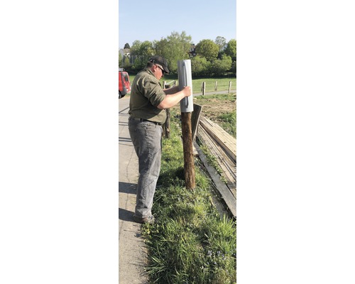 Mann befestigt einen Pfostenschuh an einem Holzpfosten im Garten