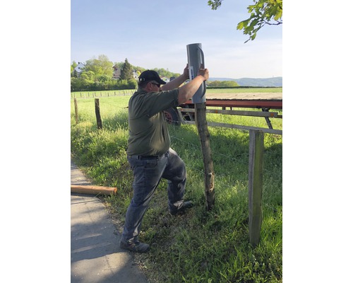 Eine Person befestigt einen Pfostenträger an einem Zaunpfahl im Aussenbereich.