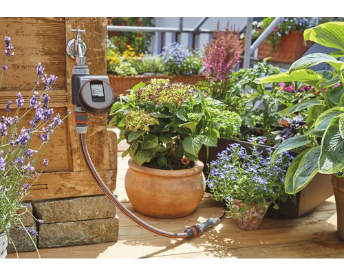 Gardena Wasserhahn mit Bewässerungssteuerung und Gartenschlauch vor bepflanztem Garten