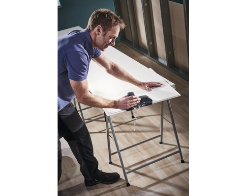 Ein Mann schneidet eine Gipskartonplatte mit einem Werkzeug auf einem Arbeitstisch.