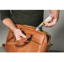 Eine Person repariert eine braune Ledertasche mit UHU Turbo Fix 2 Kleber.