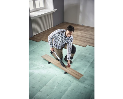 Mann schneidet Laminat mit Laminatschneider auf Dämmunterlage im Raum