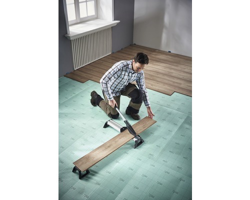 Mann schneidet Laminat mit Laminatschneider auf Trittschalldämmung