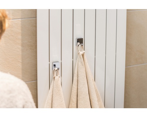 Weißer Heizkörper mit zwei Handtüchern und Chromhaken im Badezimmer.