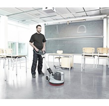 Ein Mann reinigt einen Raum mit einer Reinigungsmaschine, Tische und Stühle sind im Hintergrund zu sehen.