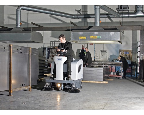 Aufsitzkehrmaschine in einer Werkshalle mit einem Mann, der sie bedient