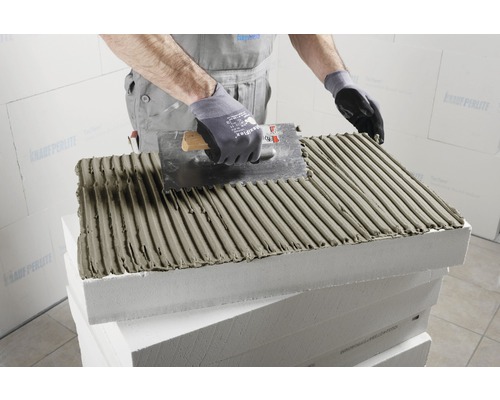 Handwerker trägt Kleber auf Dämmplatte mit einer Glättekelle auf