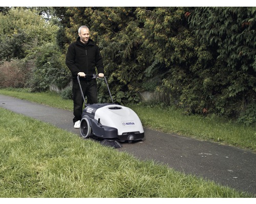 Mann schiebt Nilfisk Kehrmaschine auf einem Weg im Freien