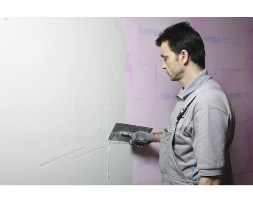 Ein Mann trägt Putz auf eine Wand auf.