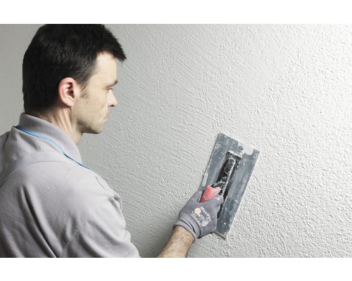 Mann verputzt Wand mit Traufel