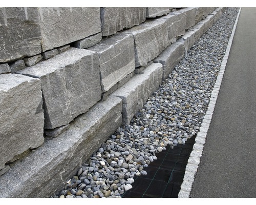 Eine Mauer aus Natursteinen mit Kiesbeet