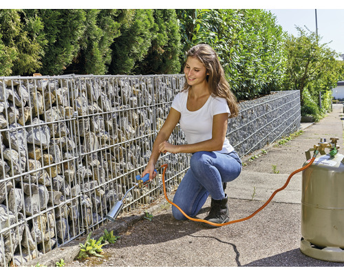 Frau entfernt Unkraut mit einem Gasbrenner an einer Gabionenwand