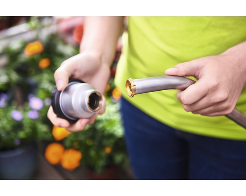 Eine Person verbindet einen Metallgartenschlauch mit einem Bewässerungsaufsatz.