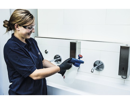 Frau sprüht Reinigungsmittel aus einer Sprühflasche auf einen Wasserhahn