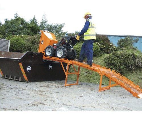 Eine Person bedient einen Mini-Dumper, der über eine Rampe in einen Container entleert wird.