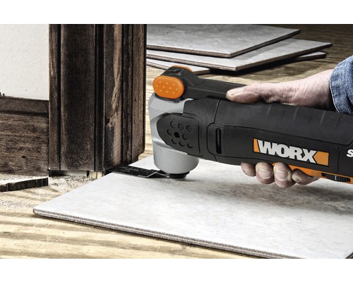 Eine Person verwendet ein Multifunktionswerkzeug von WORX, um eine Fliese neben einem Holzrahmen zu schneiden.