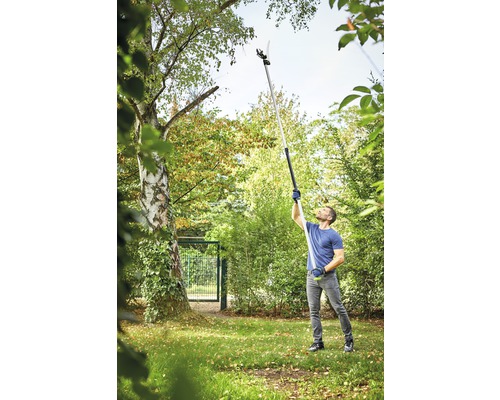Mann benutzt eine Hochentaster im Garten, um Äste von einem Baum zu schneiden.