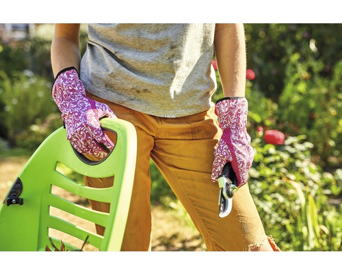 Frau mit Gartenhandschuhen, Gartenschere und Schubkarre im Garten.