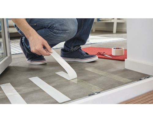 Eine Person bringt Klebeband auf dem Boden an, um Renovierungsarbeiten vorzubereiten.