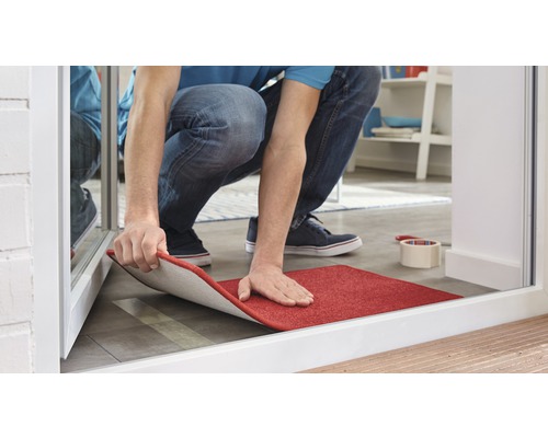 Ein Mann verlegt einen roten Teppich im Eingangsbereich.