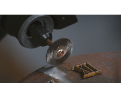 Drahtbürstenaufsatz an einer Bohrmaschine beim Entrosten eines Metallstücks