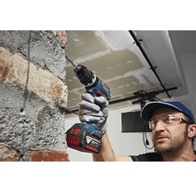 Ein Handwerker bohrt mit einem Akku-Bohrschrauber ein Loch in eine Ziegelsteinmauer.