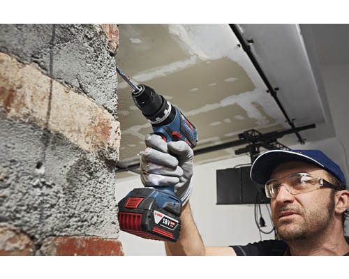 Ein Handwerker bohrt mit einem Akku-Bohrschrauber ein Loch in eine Ziegelsteinmauer.