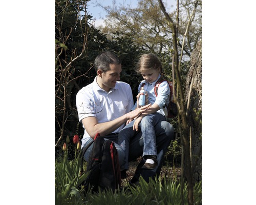 Vater trägt Insektenspray auf den Arm seiner Tochter auf, während sie im Freien sitzen.