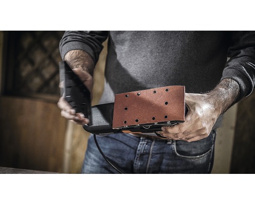 Ein Mann hält einen Schwingschleifer bereit für die Arbeit.