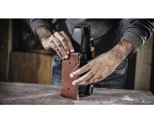 Eine Person wechselt Schleifpapier an einem Bandschleifer.