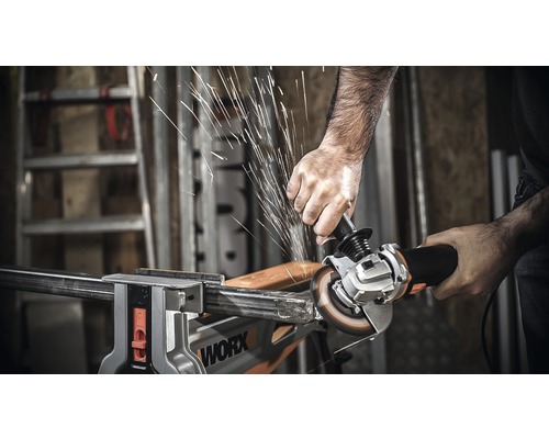 Eine Person schneidet mit einem Winkelschleifer ein Metallstück, das in einem Schraubstock fixiert ist. Es entstehen Funken.