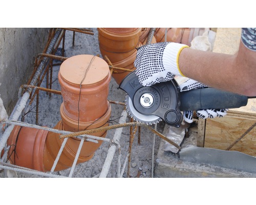 Eine Person schneidet mit einer Trennscheibe Bewehrungsstahl in einer Baugrube.