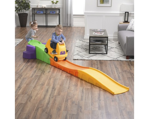 Kind auf einem gelben Step2 Achterbahnwagen auf einer bunten Achterbahn im Wohnzimmer.